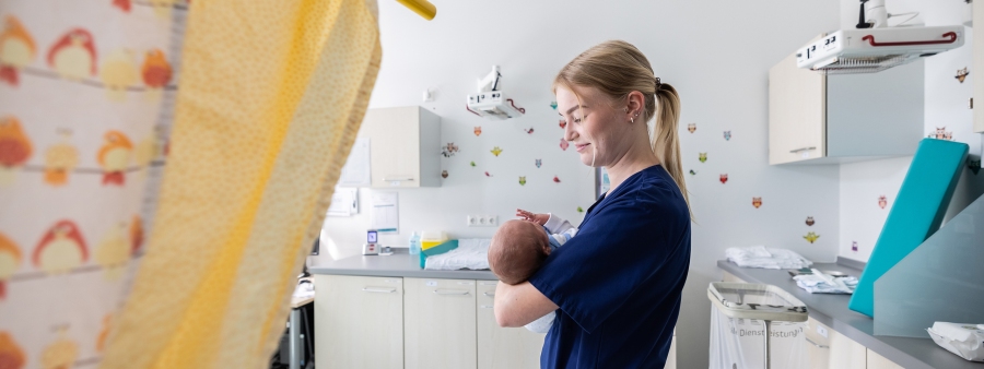 Kinderkrankenschwester im Untersuchungszimmer der Wochenbettstation mit Baby im Arm