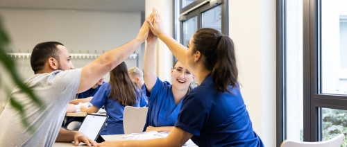 Azubis sitzen am Tisch zusammen und klatschen mit den Händen ein